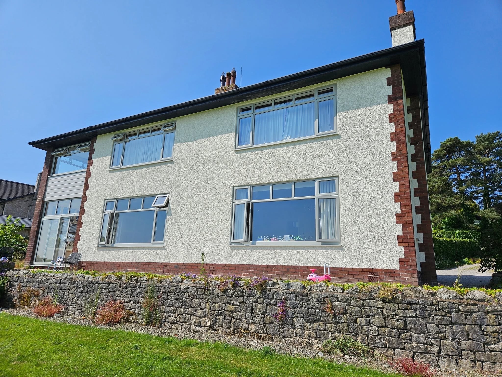 The same sandstone-quoined house from the front, behind a dry-stone wall