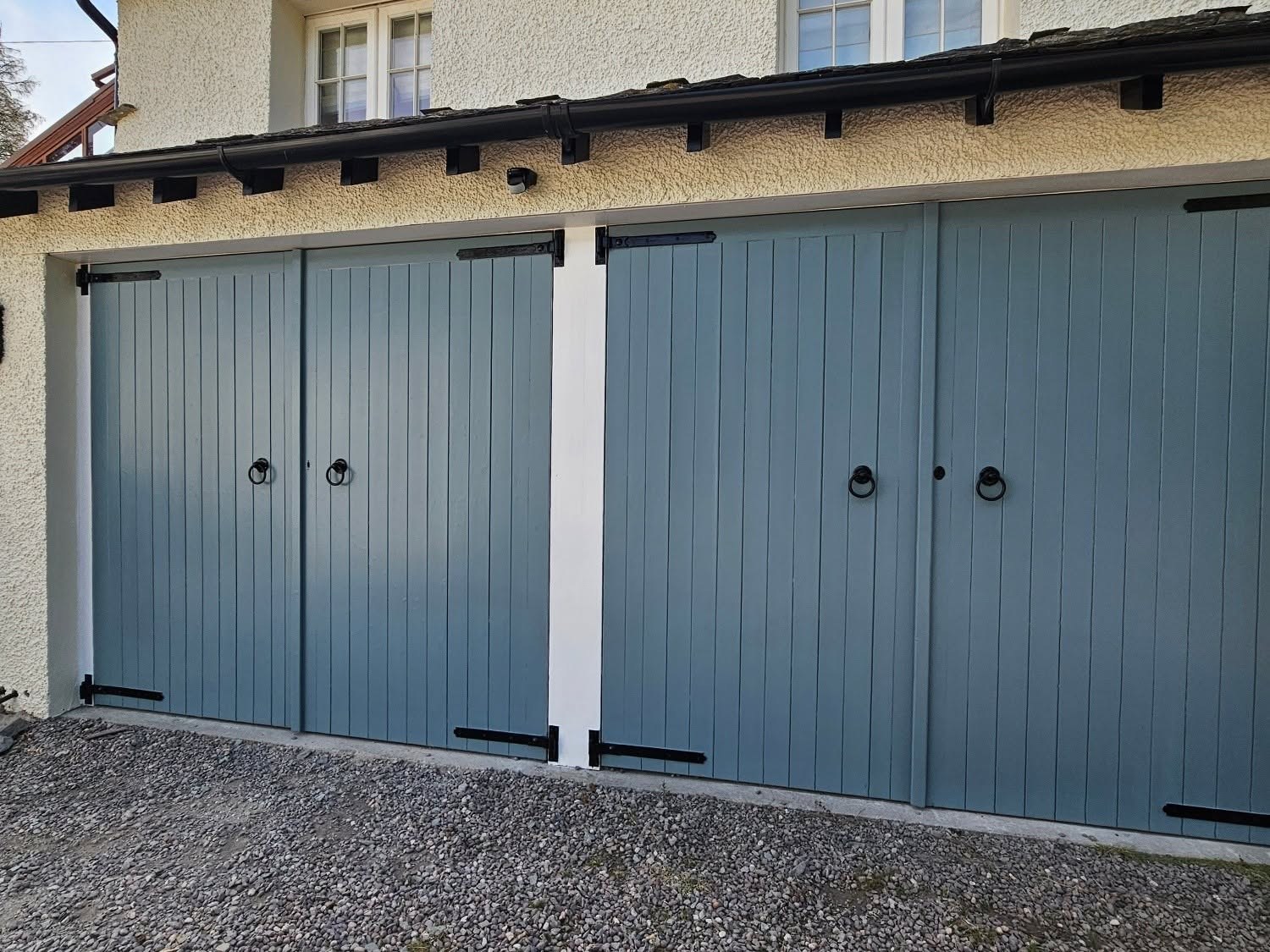 Double timber garage doors painted blue-grey with black ring handles