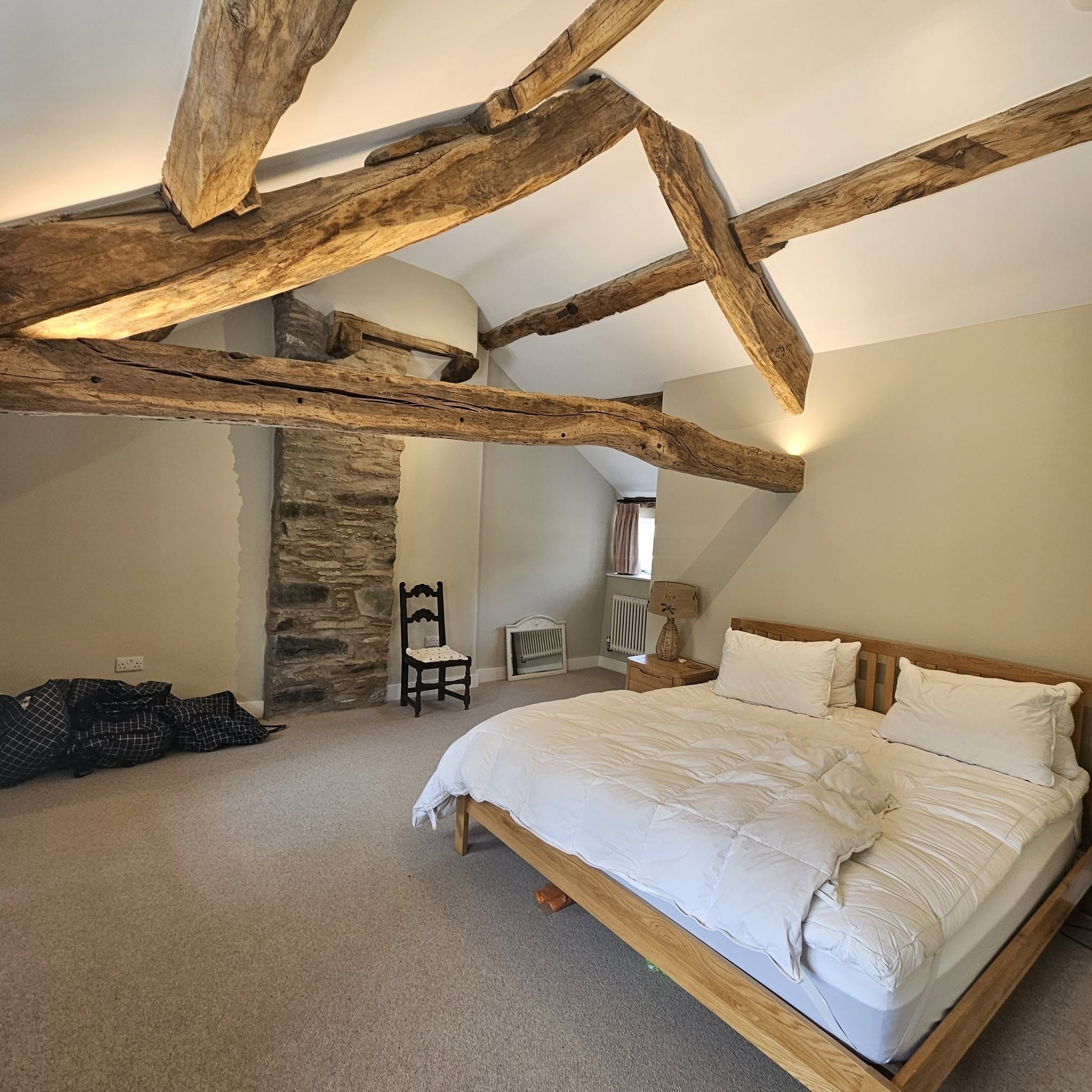 Bedroom with exposed oak trusses and a stone chimney breast, freshly decorated