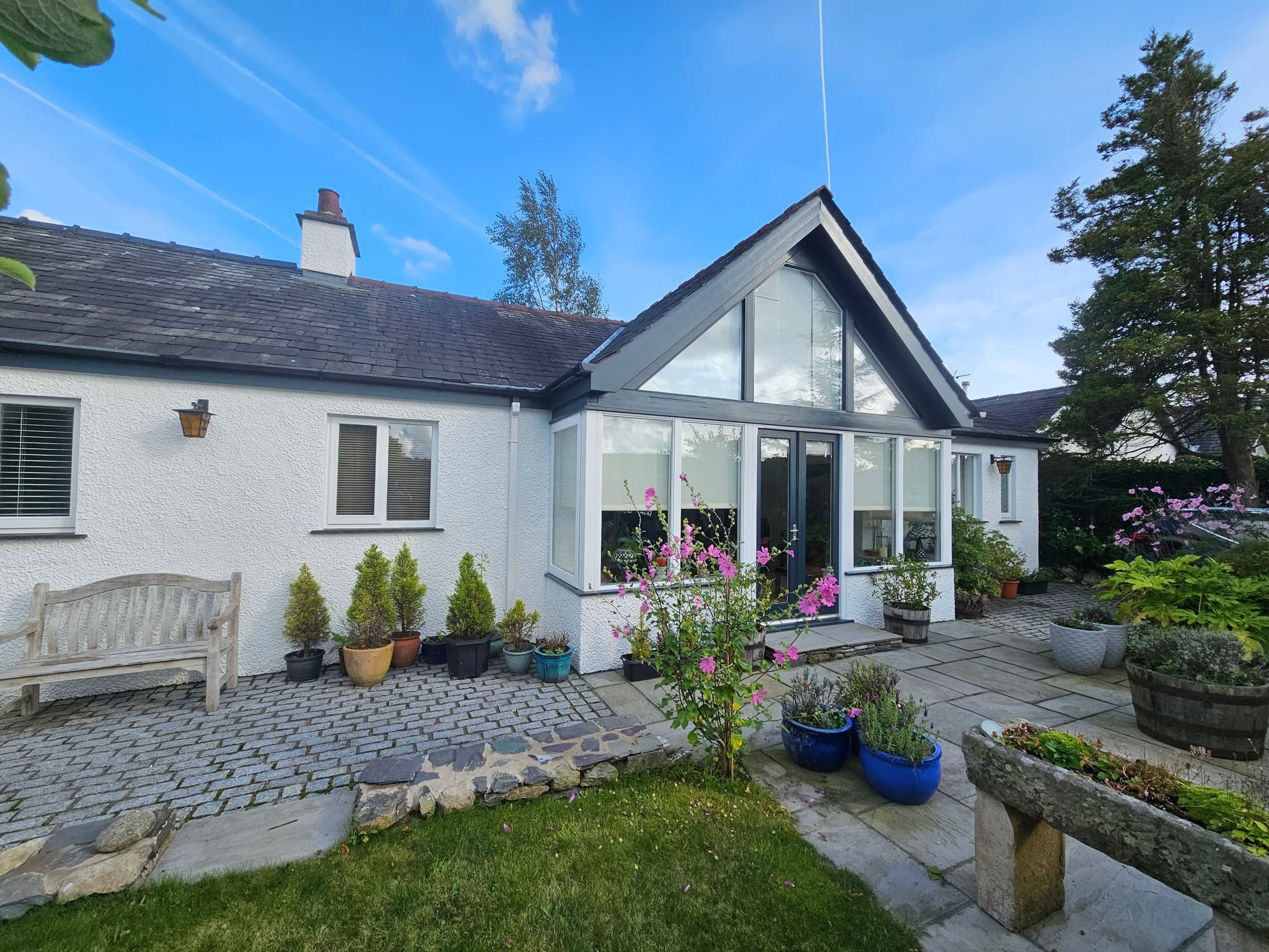 White cottage with a glazed gable garden room, cobbled patio and pots, freshly painted