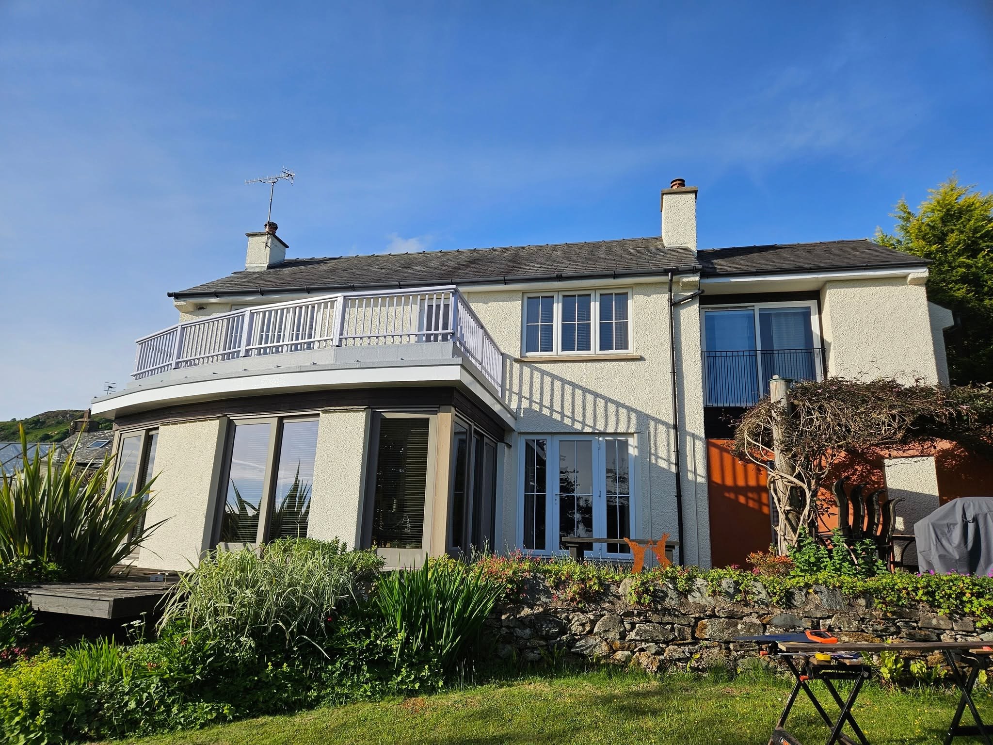 Cream rendered house with a curved balcony and white balustrade above the garden