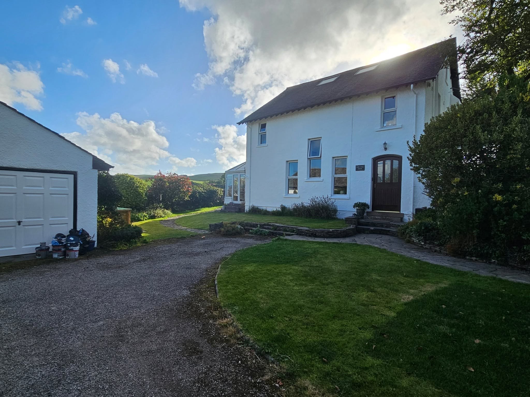 White house at the end of a gravel drive, with lawn and garage