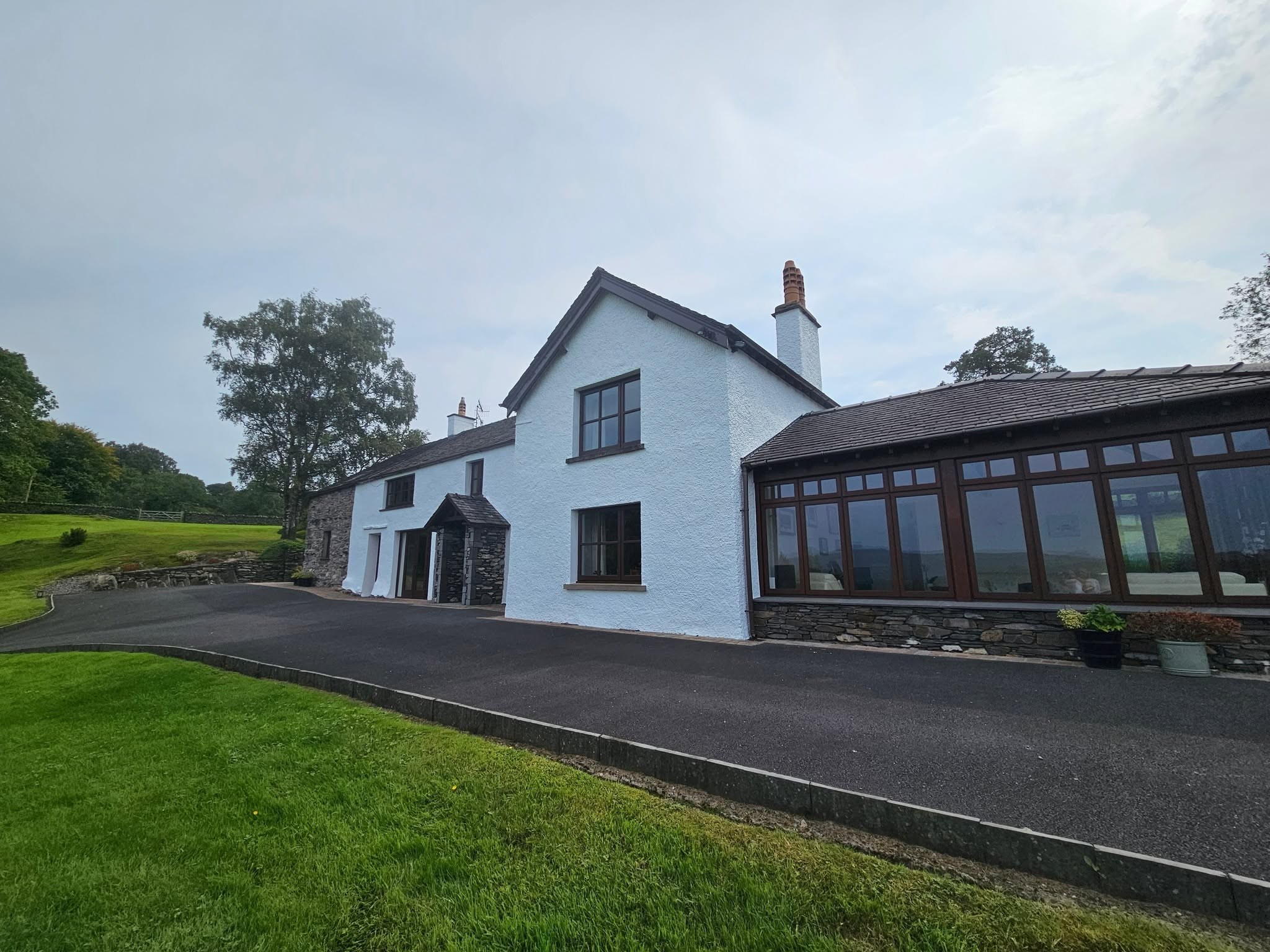Long white farmhouse with a timber conservatory, tarmac drive and lawn